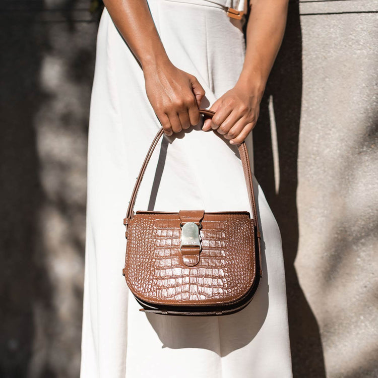 woman with black hair wearing an all white outfit with a brown croc bag holding the straps by hand