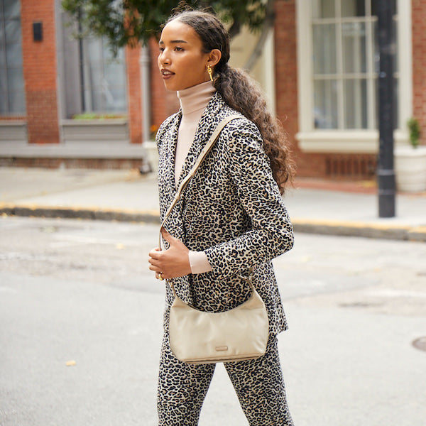 Woman with Light Brown Skin and long curly hair pulled into a ponytail wearing a patterned suit and Rose Pink Turtleneck Wearing the Strati Sporta Nylon Beech on Shoulder
