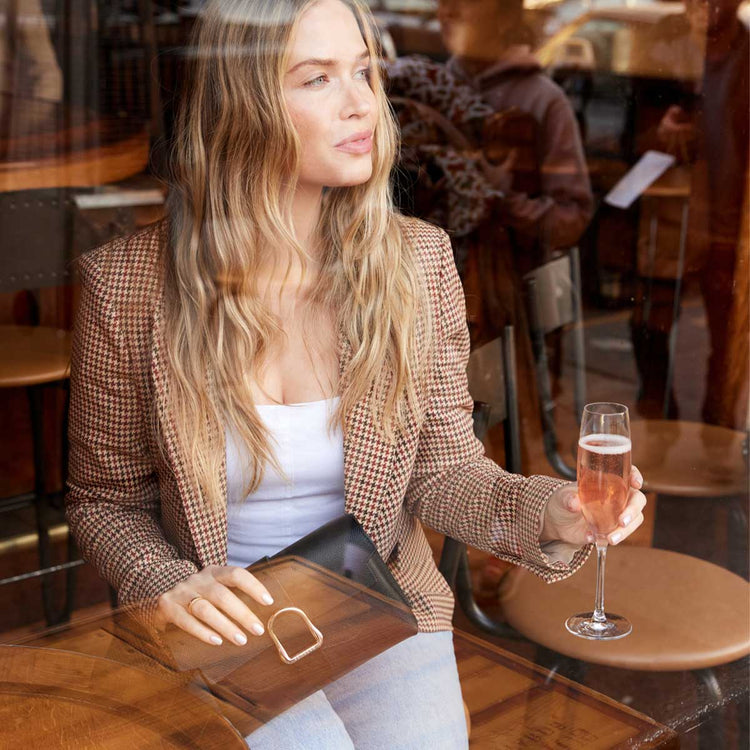 blond woman drinking a glass of champagne with black leather bag