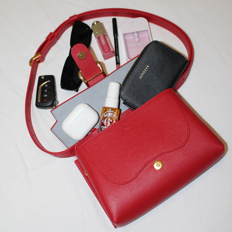red belt bag opened up with contents spilling out, including a wallet, sunglasses, keys, and more