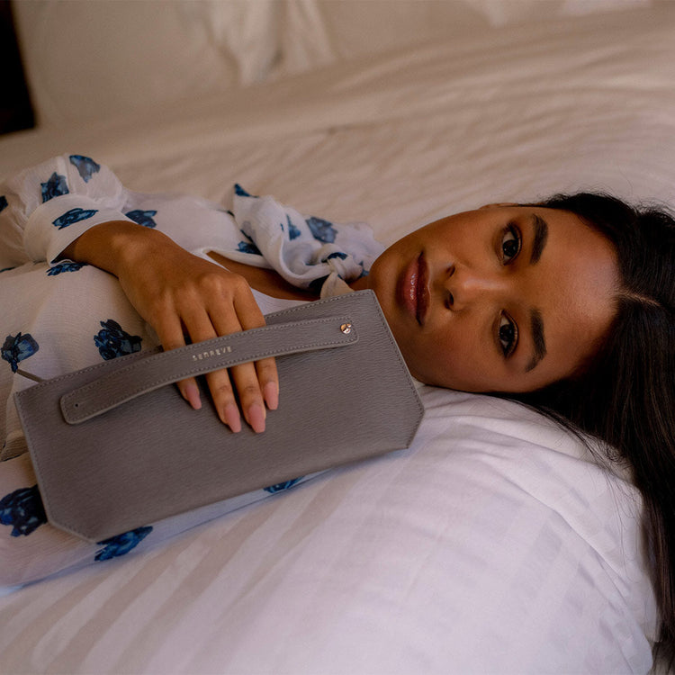 woman laying on bed holding a clutch through the handle