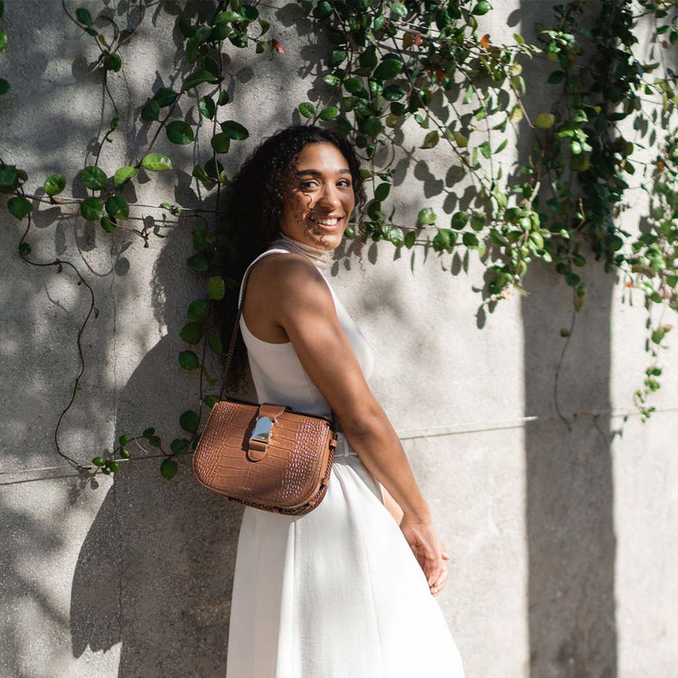 woman with black hair wearing an all white outfit with a brown croc bag worn over her shoulder with enamel chain