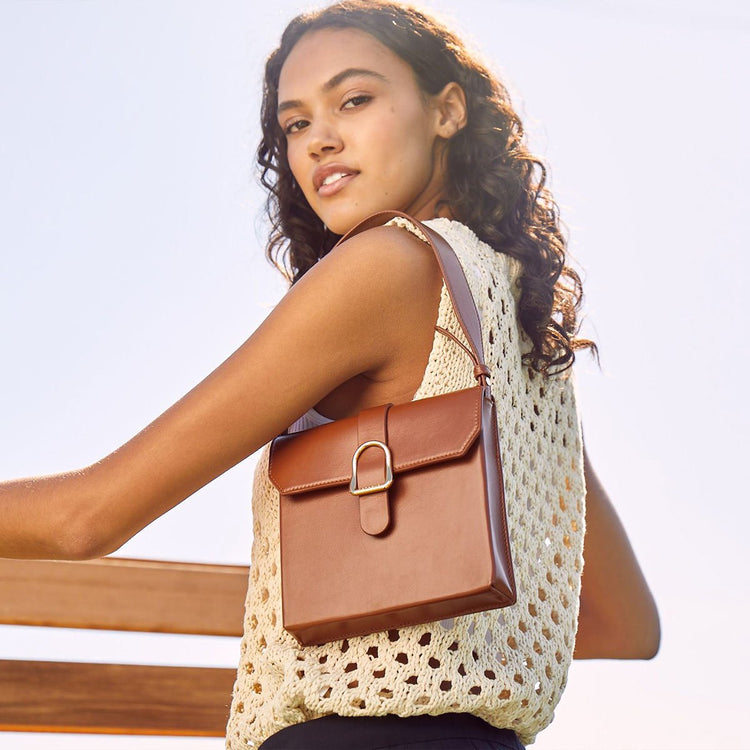 woman with brown curly hair wearing a white knit shit and a small handbag over the shoulder
