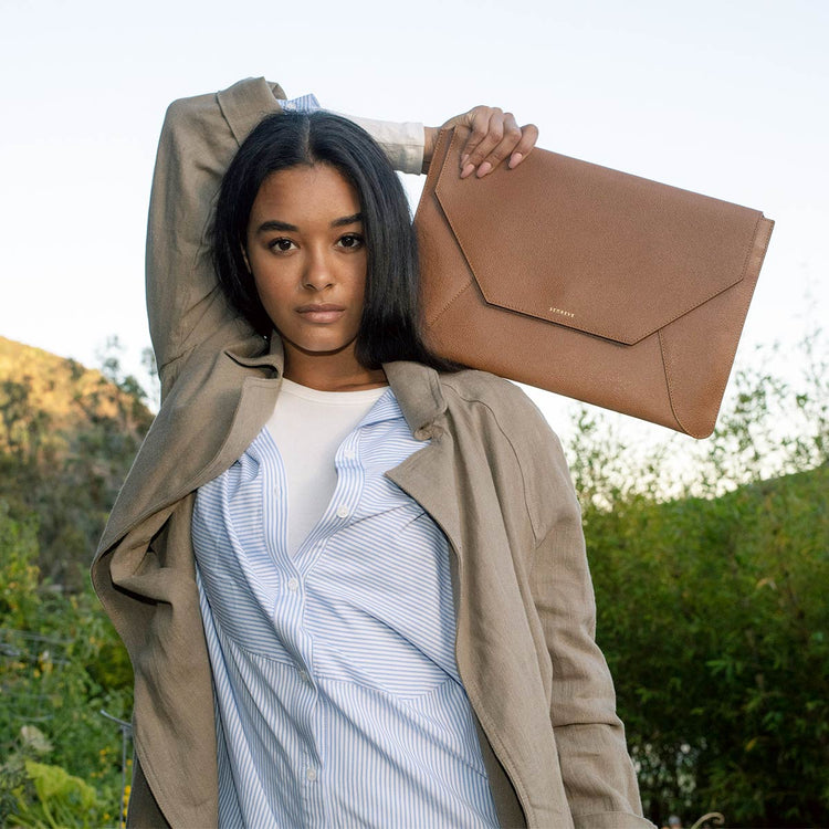 dark haired woman holding a laptop sleeve on her shoulder behind her back