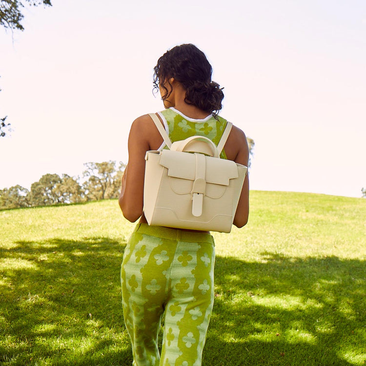 Woman in green outfit wearing Midi Maestra as a backpack walking in a bright green field