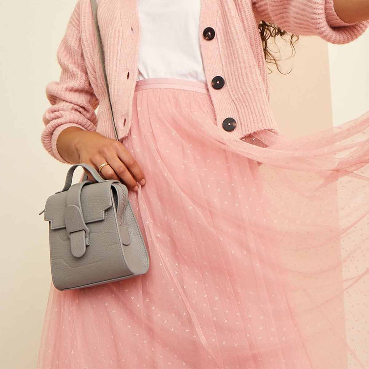 Model wearing light pink cardigan and long tool skirt wears Mini Alunna Bag in Dolce Dove as shoulder bag