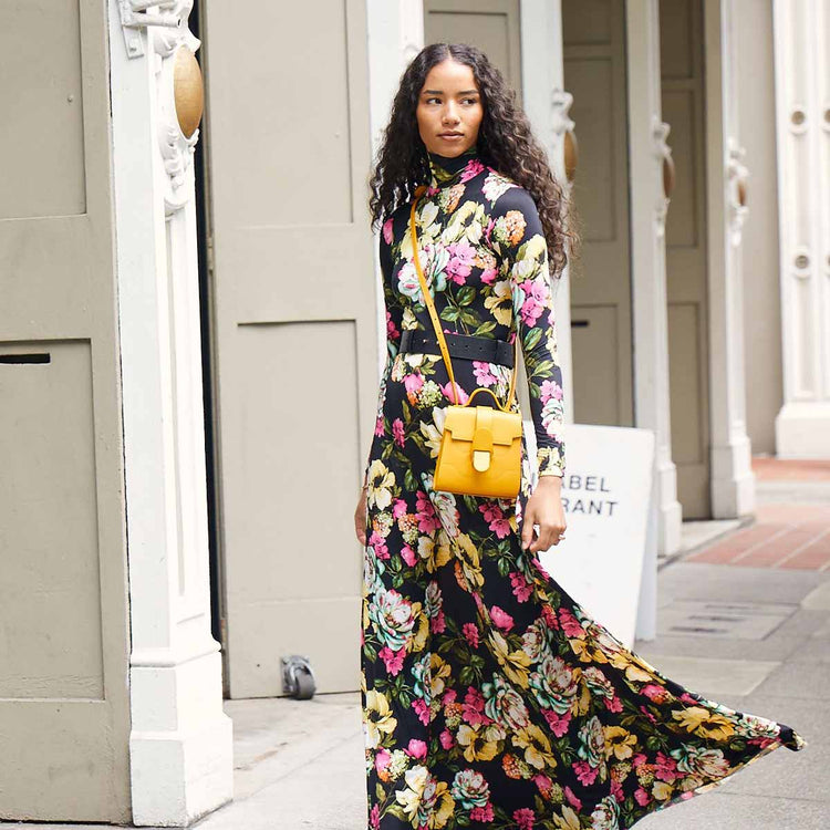 Model in long floral dress wears Mini Alunna Bag in Turmeric with Gold Hardware as a crossbody bag