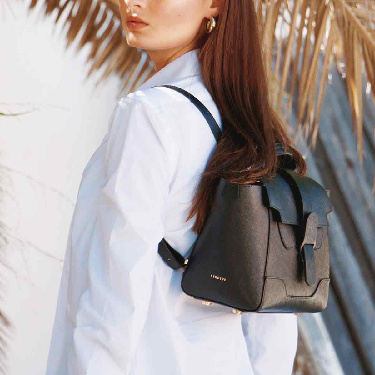 Model in crisp white collared shirt wears Pebbled Noir Mini Maestra as backpack