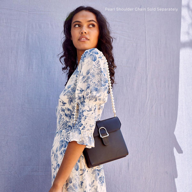 woman wearing a blue floral dress with a black saddle bag over her shoulder with a pearl chain