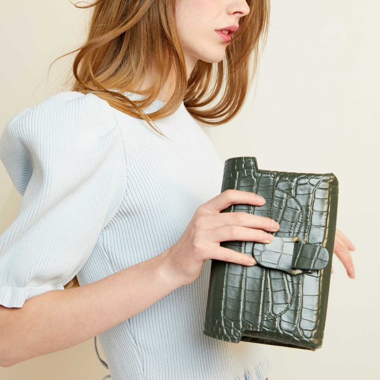 red haired model holding aria belt bag in dragon green as a clutch