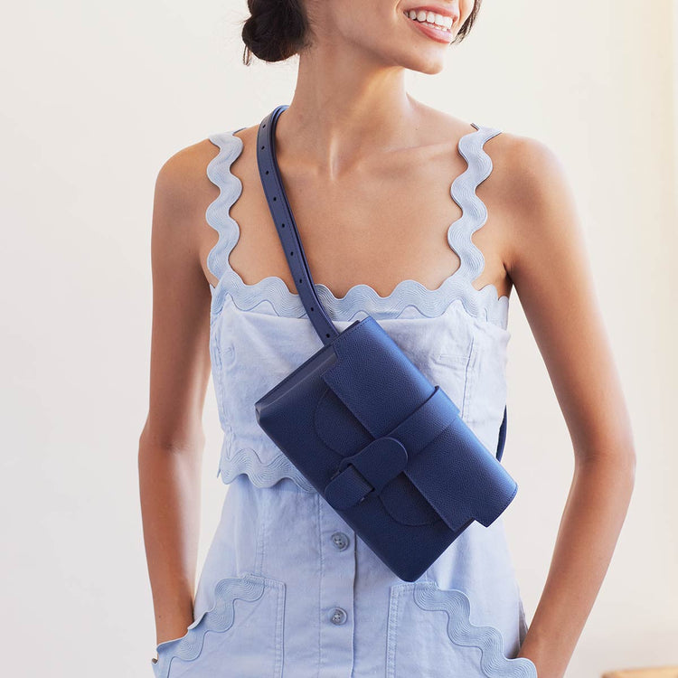 woman in light blue dress wearing marine blue belt bag as a sling