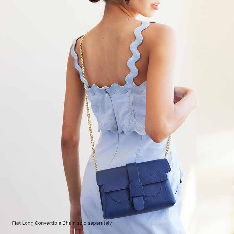 woman in light blue dress wearing marine bag with a gold chain as a crossbody