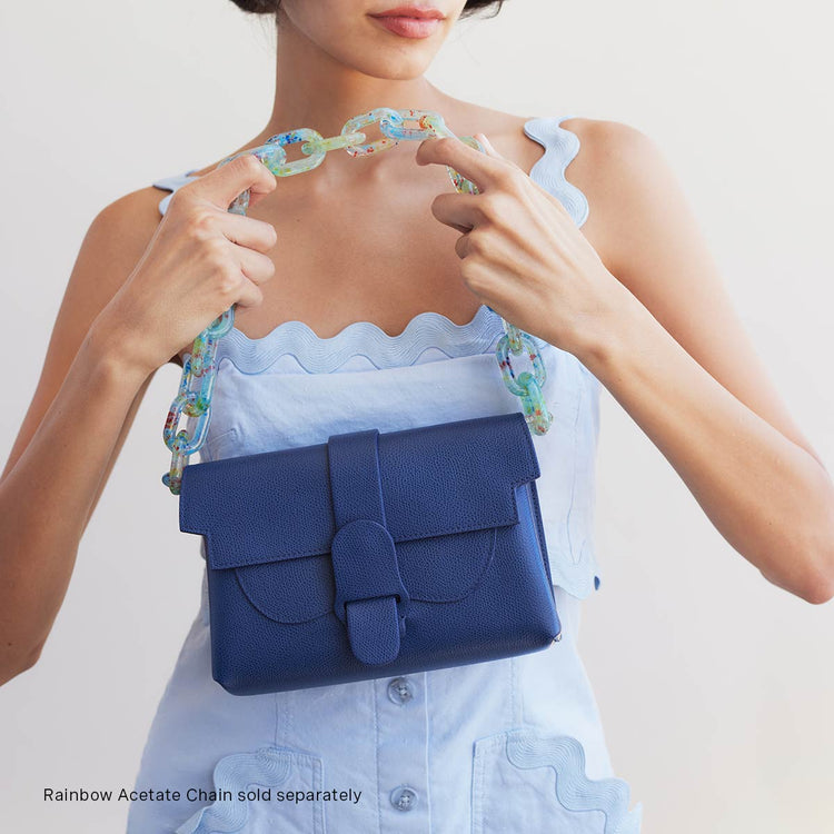 woman in light blue dress holding marine leather bag with rainbow acetate shoulder chain