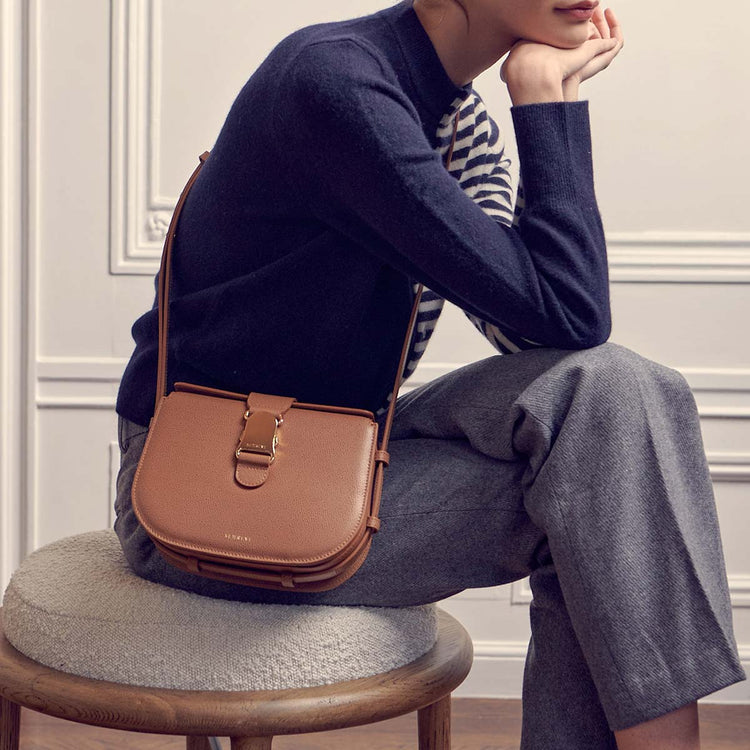 woman sitting down wearing a brown leather crossbody bag