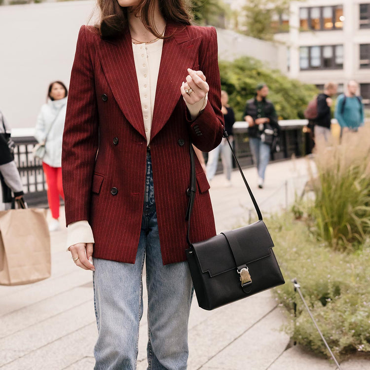 brunette with red blazer holding a black shoulder bag