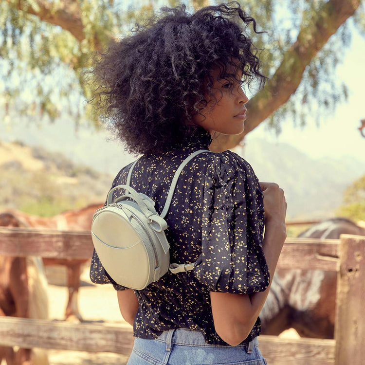 woman wearing a floral shirt wearing a white circle bag as a backpack