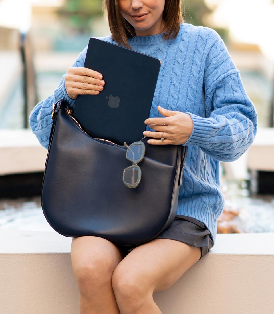 Woman in light blue sweater putting a laptop into a dark blue leather handbag