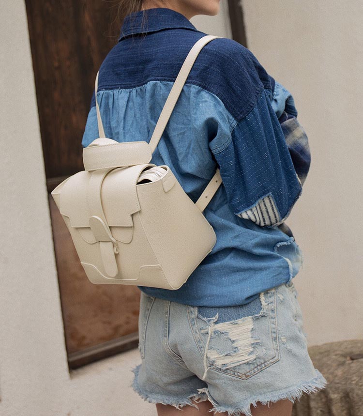 Woman wearing a denim top and shorts with the Mini Maestra in White, worn as a backpack