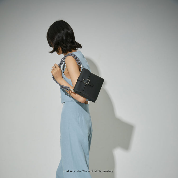 woman holding black saddle bag with an acetate chain